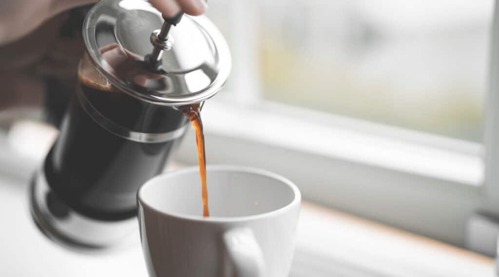 The French Press filled with espresso style coffee being poured into a cup.  