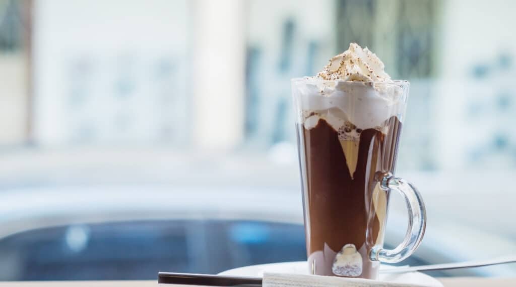 A Tall glass filled with mocha and a whipped cream topper.  